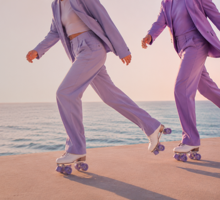 Two people rollerskating along a seafront in matching purple suits